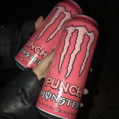 two cans of monster energy drink being held by someone