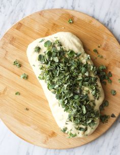 a wooden cutting board topped with bread covered in herbs