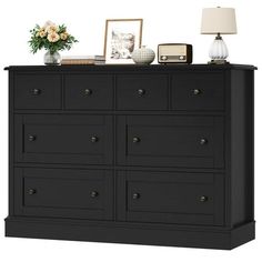 a black dresser with flowers and pictures on it's top shelf next to a lamp