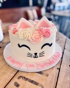 a white cake with pink frosting and flowers on top is sitting on a wooden table