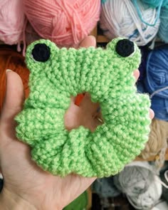 a person holding up a green crocheted object with eyes on it's face