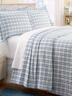 a bed with blue and white plaid comforter in a bedroom next to a window