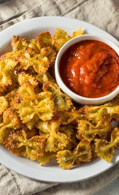 a white plate topped with fried food next to a bowl of sauce