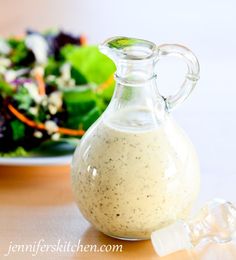 a glass bottle filled with dressing sitting next to a plate of salad on a table