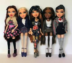 five dolls standing next to each other in front of a white wall and wearing clothes