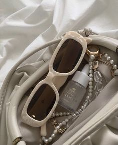 the contents of a purse are laid out on a white sheet, including sunglasses and jewelry