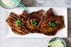 three pieces of meat on a plate with chopsticks next to it and rice