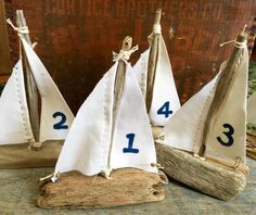 three sailboats made out of driftwood are sitting on a table with numbers painted on them