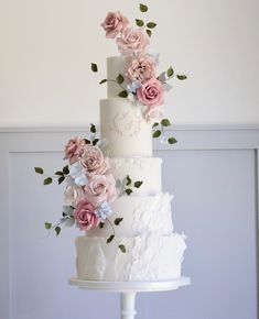 a three tiered wedding cake with pink and white flowers on the top, sitting on a pedestal