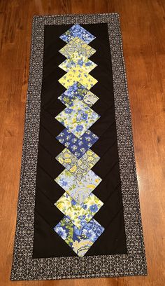 a quilted table runner with blue and yellow flowers on the border, sitting on a wooden floor