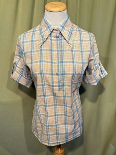 "This is an adorable vintage blouse from the 70s or so. Labeled Lucky Pierre. No size tag. The bust measures 34\" with measurements below. Made of a blue & white cotton blend in a plaid pattern. The pullover blouse closes down the front bodice with plastic buttons. The blouse has elbow length sleeves cuffed up with buttons and tabs. Hem is straight. It is hip length.   The blouse is in very good condition!  No damage. No stains or soil. Super cute!  If you have never worn vintage before, please Retro Collared Top For Work, Retro Blue Blouse For Workwear, Retro Blue Blouse For Work, Blue Retro Blouse For Work, Vintage Blue Tops For Workwear, 1970s Collared Tops For Spring, Blue Retro Collared Tops, Blue Collared Retro Tops, Retro Blue Collared Top