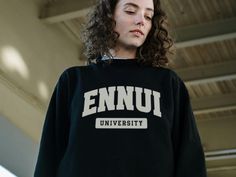 Feeling listless and dissatisfied with the world? Join the club at Ennui University! This cozy, light-weight crewneck sweatshirt features a bold, collegiate-style graphic across the chest that says "Ennui University" - a playful nod to the existential crisis we're all experiencing. Crafted from soft 100% ringspun cotton, it's the perfect comfy-yet-stylish way to embrace your ennui with a wink and a smile. Whether you're a disillusioned college student or just someone who was promised the American Dream but got crushed under the weight of capitalism, this sweatshirt lets you wear your angst on your sleeve (literally) while maintaining a sense of humor. Machine washable and built to last, it's a cozy reminder that we're all in this together, even if life feels a bit aimless sometimes. Produc Crew Neck T-shirt With University Logo For Fall, University Logo Long Sleeve Tops For Streetwear, Black Crew Neck Sweatshirt For Campus, Campus Text Print Crew Neck Sweatshirt, Crew Neck Sweatshirt With Text Print For Campus, Collegiate Streetwear Sweatshirt With Text Print, Varsity Style Long Sleeve T-shirt With University Logo, Varsity Long Sleeve T-shirt With University Logo, Long Sleeve College Style Top With University Logo