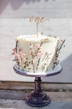 a white cake with pink flowers and the number one on top is sitting on a plate