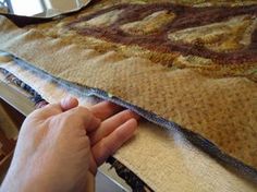 a hand is holding the edge of a piece of fabric on top of a table