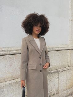 a woman with an umbrella standing in front of a white wall wearing a long coat