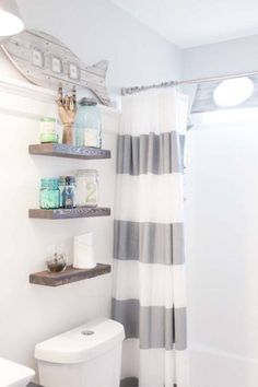 a white toilet sitting next to a bath tub under a bathroom mirror with shelves above it