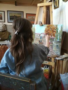 a woman sitting in front of an easel painting