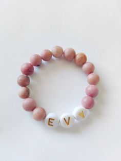 "*This is a single bracelet with pink stone beads and a custom word of your choosing. Letter beads have two colors: Gold and black. SIZING: 3.5\" PREEMIE/SMALL NEWBORN 4\"NEWBORN-5MONTH 4.5\" 6-12 MONTH 5\" 1 YEAR SIZING IS JUST A GUIDE. IT IS BEST TO MEASURE FOR BEST ACCURACY. Take a sting and loop it around your babies wrist, leave a bit of wiggle room and measure to a tape measure or ruler. *Handmade item *Can be personalized Stretch and elastic fit. Customizable worded bracelet stacks. Perfe Spiritual Pink Jewelry For Birthday, Customizable Pink Bracelet Jewelry, Personalized Pink Spiritual Bracelets, Personalized Pink Spiritual Bracelet, Spiritual Personalized Pink Bracelets, Spiritual Pink Personalized Bracelets, Spiritual Personalized Pink Bracelet, Spiritual Pink Bracelets For Everyday, Pink Beaded Name Bracelet For Birthday