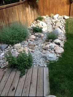 a small garden with rocks and plants in the middle, along side a wooden fence