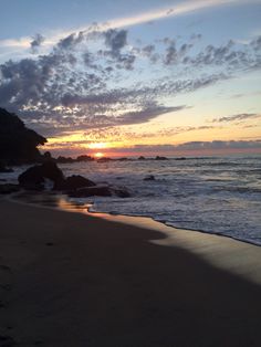 the sun is setting over the ocean with rocks in the foreground and water on the beach