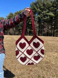 a woman is holding a crocheted bag with hearts on it