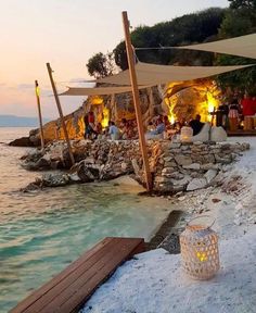 an outdoor dining area next to the ocean at dusk with people sitting around tables and umbrellas