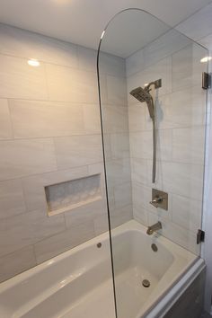 a bath tub sitting next to a shower head in a white tiled bathroom with a glass door