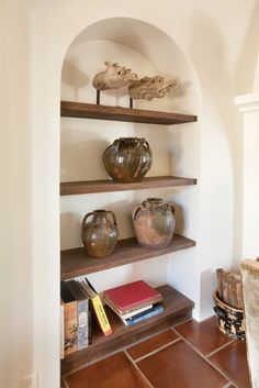 some shelves with vases and books on them in a room that has tile flooring