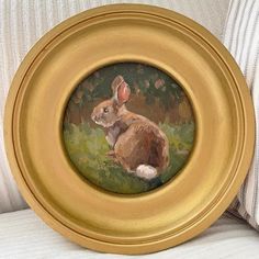 a painting of a rabbit in a gold frame sitting on a white couch next to a striped pillow