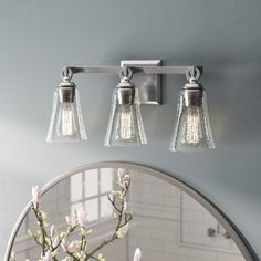 three light bathroom fixture with clear glass shades on the top and bottom, over a mirror