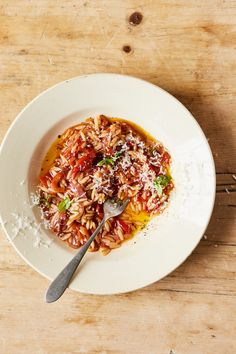 a white bowl filled with rice and sauce on top of a wooden table next to a spoon