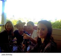 four people sitting at a table with wine glasses in front of them and smiling for the camera