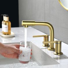 a person's hand holding a glass with water coming out of it in front of a faucet