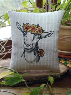 a pillow with a cow's head and flowers on it sitting next to a potted plant