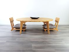 a wooden table with two chairs and a black bowl on top of it, in front of a white wall