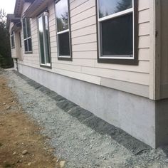 the side of a house that is being built with concrete and gravel on the ground