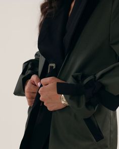 Elevate your trench game with our Ember Trench Coat, made from the softest deadstock cotton in a mix black and olive green. Featuring chic wide lapels, tortoise shell buttons, and convenient welt pockets for when you don’t know what to do with your hands. Its hidden detachable belt offers a tailored fit, making it the ideal versatile fashion statement your closet needs.This sustainable trench coat is tailor made and on demand and takes us 7 hours to make it. Please allow 1-5 business days for pr Green Military Style Workwear Outerwear, Green Military Style Outerwear For Work, Military Style Green Outerwear For Work, Green Outerwear With Belted Cuffs And Long Sleeves, Green Outerwear With Button Cuffs For Work, Green Long Sleeve Outerwear With Belted Cuffs, Olive Blazer For Fall Workwear, Green Long Coat Blazer For Workwear, Military Style Fall Blazer For Workwear