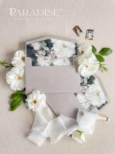 the wedding stationery is laid out on the floor with white flowers and greenery