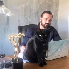 a man sitting in front of a laptop computer with a black cat on his lap