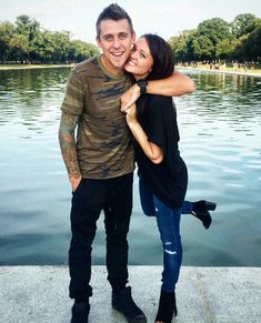 a man and woman standing next to each other in front of a body of water