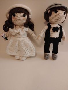 two crocheted dolls holding hands on a white surface with one wearing a hat and the other in a dress