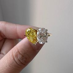 a woman's hand holding an engagement ring with two yellow and white diamonds on it