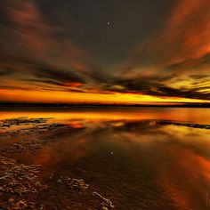 an orange and yellow sunset over the ocean with clouds in the sky, reflecting on the water's surface