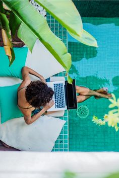 a woman sitting on the edge of a swimming pool using her laptop