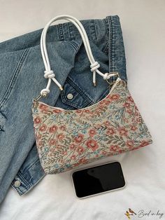 a purse and cell phone sitting on top of a white bed next to blue jeans