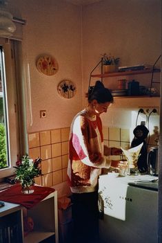 a woman standing in a kitchen preparing food on top of a stove next to a window