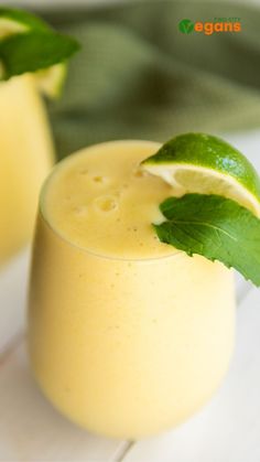 two glasses filled with yellow liquid and garnished with green leaves