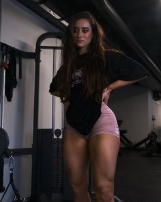 a woman in pink shorts standing next to a gym equipment rack and exercise machine with her hands on her hips