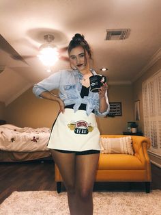 a woman standing in a room with an apron on and holding a camera up to her chest