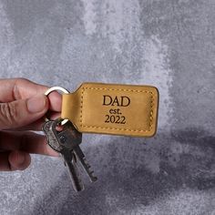 a hand holding a leather keychain with the word dad est 2022 engraved on it